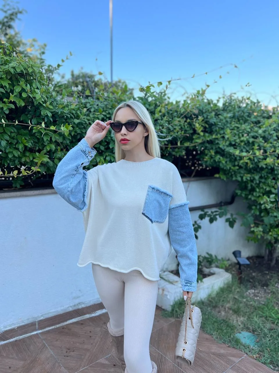 Denim detaylı triko kazak giyen, bordo tayt ve kürklü çizmelerle kombin yapan bir kadın. Kazak ekru rengiyle sade ve şık bir görünüm sunuyor.