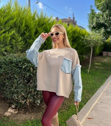 Denim detaylı triko kazak giyen, bordo tayt ve kürklü çizmelerle kombin yapan bir kadın. Kazak ekru rengiyle sade ve şık bir görünüm sunuyor.