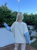 Denim detaylı triko kazak giyen, bordo tayt ve kürklü çizmelerle kombin yapan bir kadın. Kazak ekru rengiyle sade ve şık bir görünüm sunuyor.