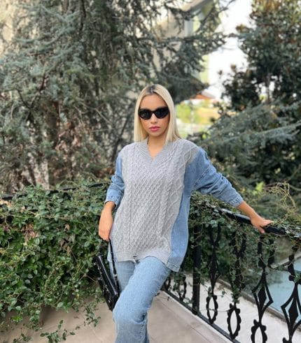 Denim kollu, örgü desenli krem renkli triko kazak giyen bir kadın, beyaz pantolon ve şık aksesuarlarla günlük kombinini tamamlıyor.