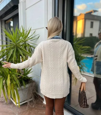 Dış mekânda beyaz triko hırka, kahverengi deri tokalı detaylar, mavi denim elbise ve kahverengi deri çizmelerle kombinlenmiş bir kadın modeli.