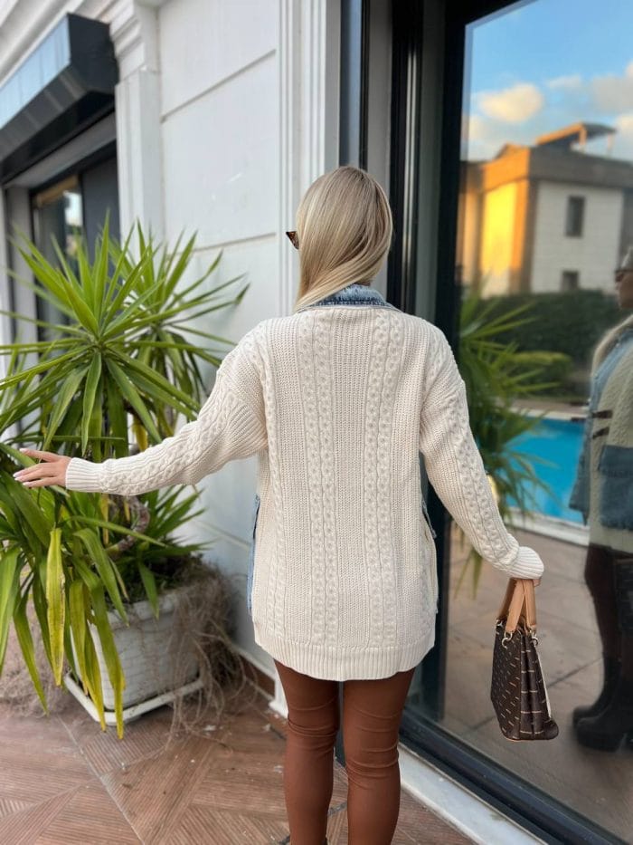 Dış mekânda beyaz triko hırka, kahverengi deri tokalı detaylar, mavi denim elbise ve kahverengi deri çizmelerle kombinlenmiş bir kadın modeli.