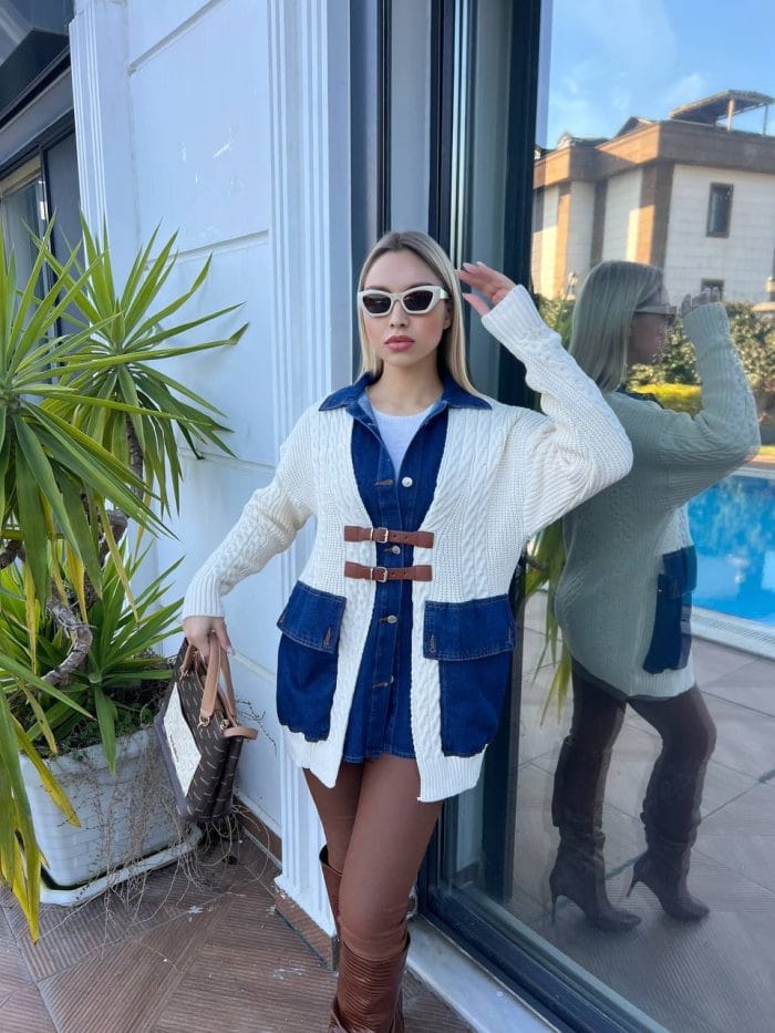 Dış mekânda beyaz triko hırka, kahverengi deri tokalı detaylar, mavi denim elbise ve kahverengi deri çizmelerle kombinlenmiş bir kadın modeli.