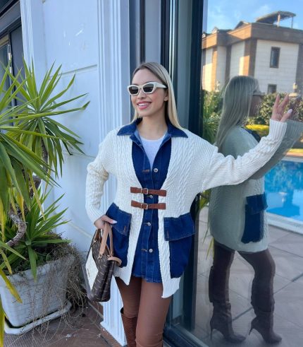 Dış mekânda beyaz triko hırka, kahverengi deri tokalı detaylar, mavi denim elbise ve kahverengi deri çizmelerle kombinlenmiş bir kadın modeli.