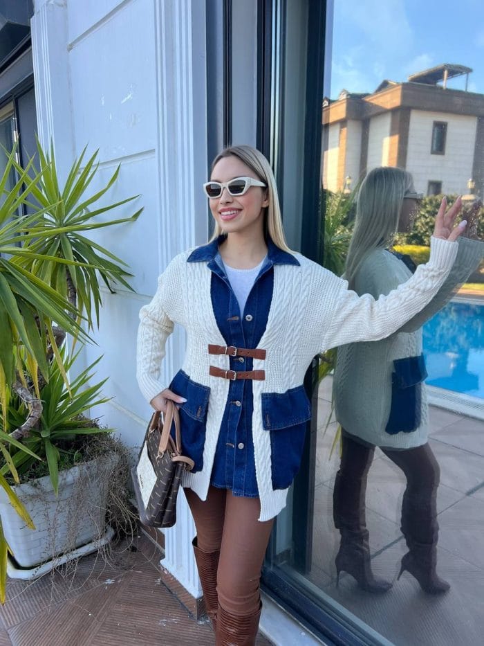 Dış mekânda beyaz triko hırka, kahverengi deri tokalı detaylar, mavi denim elbise ve kahverengi deri çizmelerle kombinlenmiş bir kadın modeli.