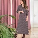 bordo ve beyaz desenli uzun kollu elbise giymiş bir kadın; belinde bağlama detayı ve kahverengi topuklu botlar.