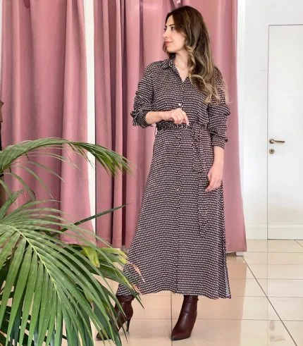 bordo ve beyaz desenli uzun kollu elbise giymiş bir kadın; belinde bağlama detayı ve kahverengi topuklu botlar.
