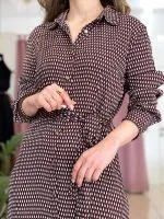 bordo ve beyaz desenli uzun kollu elbise giymiş bir kadın; belinde bağlama detayı ve kahverengi topuklu botlar.