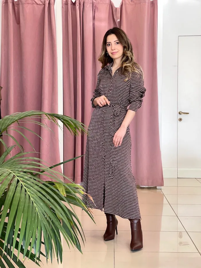 bordo ve beyaz desenli uzun kollu elbise giymiş bir kadın; belinde bağlama detayı ve kahverengi topuklu botlar.