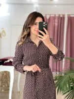 bordo ve beyaz desenli uzun kollu elbise giymiş bir kadın; belinde bağlama detayı ve kahverengi topuklu botlar.