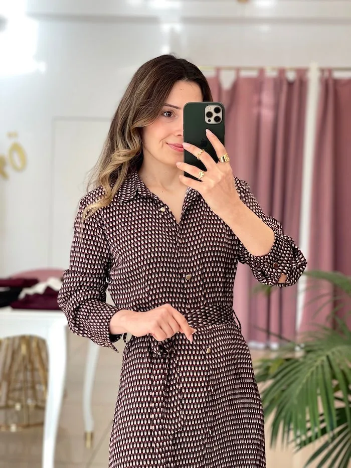 bordo ve beyaz desenli uzun kollu elbise giymiş bir kadın; belinde bağlama detayı ve kahverengi topuklu botlar.