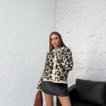 Leopar desenli düğmeli hırka giyen bir kadın. Hırka siyah deri etek, kahverengi bir çanta ve siyah çizmelerle kombinlenmiş.