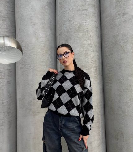 Ella Style lacivert baklava desenli oversize triko kazak giyen bir kadın. Kazağı, yırtık kot pantolon ve kırmızı detaylı bir çantayla kombinlemiş, kırmızı gözlüklerle şık bir dokunuş katmış.