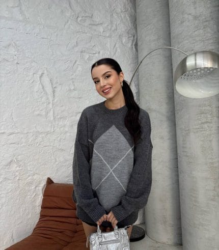 Ella Style gri baklava desenli oversize triko kazak giyen bir kadın. Kazağı siyah mini etek ve gümüş detaylı bir çantayla kombinlemiş.