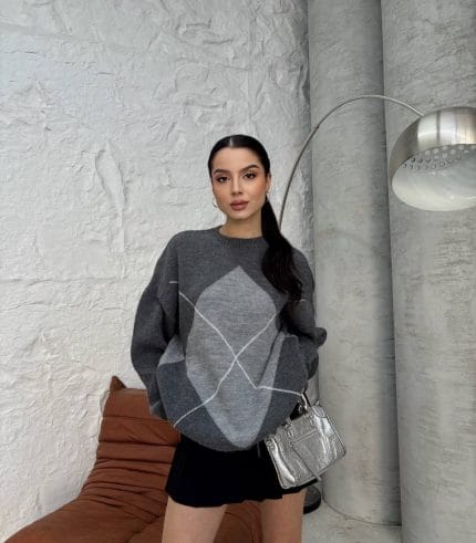 Ella Style gri baklava desenli oversize triko kazak giyen bir kadın. Kazağı siyah mini etek ve gümüş detaylı bir çantayla kombinlemiş.