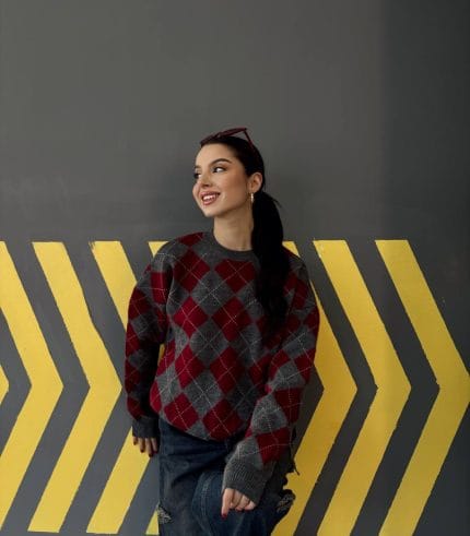 Ella Style lacivert baklava desenli oversize triko kazak giyen bir kadın. Kazağı, yırtık kot pantolon ve kırmızı detaylı bir çantayla kombinlemiş, kırmızı gözlüklerle şık bir dokunuş katmış.