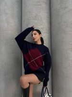 Ella Style gri baklava desenli oversize triko kazak giyen bir kadın. Kazağı siyah mini etek ve gümüş detaylı bir çantayla kombinlemiş.