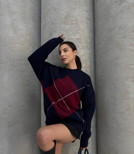 Ella Style gri baklava desenli oversize triko kazak giyen bir kadın. Kazağı siyah mini etek ve gümüş detaylı bir çantayla kombinlemiş.
