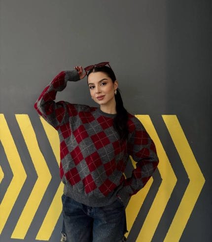 Ella Style lacivert baklava desenli oversize triko kazak giyen bir kadın. Kazağı, yırtık kot pantolon ve kırmızı detaylı bir çantayla kombinlemiş, kırmızı gözlüklerle şık bir dokunuş katmış.