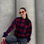 Ella Style lacivert baklava desenli oversize triko kazak giyen bir kadın. Kazağı, yırtık kot pantolon ve kırmızı detaylı bir çantayla kombinlemiş, kırmızı gözlüklerle şık bir dokunuş katmış.