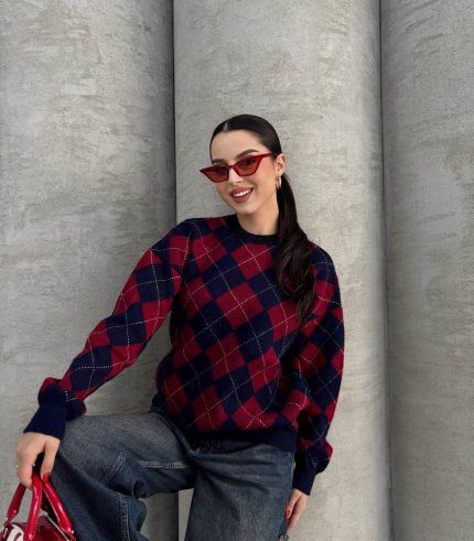 Ella Style lacivert baklava desenli oversize triko kazak giyen bir kadın. Kazağı, yırtık kot pantolon ve kırmızı detaylı bir çantayla kombinlemiş, kırmızı gözlüklerle şık bir dokunuş katmış.