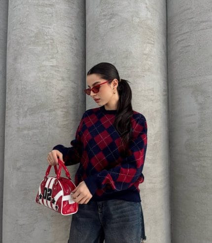 Ella Style lacivert baklava desenli oversize triko kazak giyen bir kadın. Kazağı, yırtık kot pantolon ve kırmızı detaylı bir çantayla kombinlemiş, kırmızı gözlüklerle şık bir dokunuş katmış.