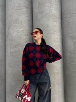 Ella Style lacivert baklava desenli oversize triko kazak giyen bir kadın. Kazağı, yırtık kot pantolon ve kırmızı detaylı bir çantayla kombinlemiş, kırmızı gözlüklerle şık bir dokunuş katmış.