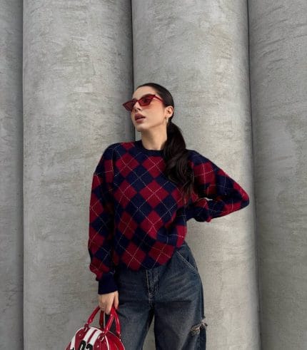 Ella Style lacivert baklava desenli oversize triko kazak giyen bir kadın. Kazağı, yırtık kot pantolon ve kırmızı detaylı bir çantayla kombinlemiş, kırmızı gözlüklerle şık bir dokunuş katmış.