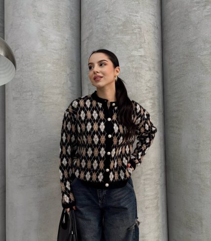 Ella Style pitikare ve baklava desenli siyah kadın hırka giyen bir kadın, bol kesim kot pantolon ve siyah çantayla kombin yapmış. Modern bir görünüm sağlayan gri beton sütunlar arka planda yer alıyor.