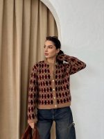 Ella Style pitikare ve baklava desenli siyah kadın hırka giyen bir kadın, bol kesim kot pantolon ve siyah çantayla kombin yapmış. Modern bir görünüm sağlayan gri beton sütunlar arka planda yer alıyor.
