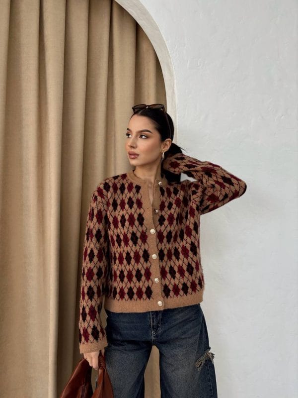 Ella Style pitikare ve baklava desenli siyah kadın hırka giyen bir kadın, bol kesim kot pantolon ve siyah çantayla kombin yapmış. Modern bir görünüm sağlayan gri beton sütunlar arka planda yer alıyor.