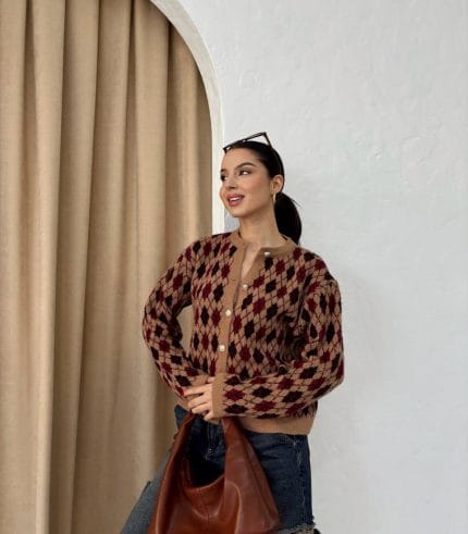 Ella Style pitikare ve baklava desenli siyah kadın hırka giyen bir kadın, bol kesim kot pantolon ve siyah çantayla kombin yapmış. Modern bir görünüm sağlayan gri beton sütunlar arka planda yer alıyor.