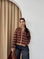 Ella Style pitikare ve baklava desenli siyah kadın hırka giyen bir kadın, bol kesim kot pantolon ve siyah çantayla kombin yapmış. Modern bir görünüm sağlayan gri beton sütunlar arka planda yer alıyor.