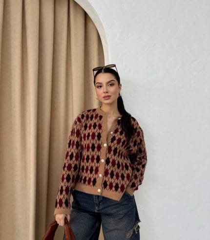 Ella Style pitikare ve baklava desenli siyah kadın hırka giyen bir kadın, bol kesim kot pantolon ve siyah çantayla kombin yapmış. Modern bir görünüm sağlayan gri beton sütunlar arka planda yer alıyor.