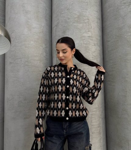 Ella Style pitikare ve baklava desenli siyah kadın hırka giyen bir kadın, bol kesim kot pantolon ve siyah çantayla kombin yapmış. Modern bir görünüm sağlayan gri beton sütunlar arka planda yer alıyor.