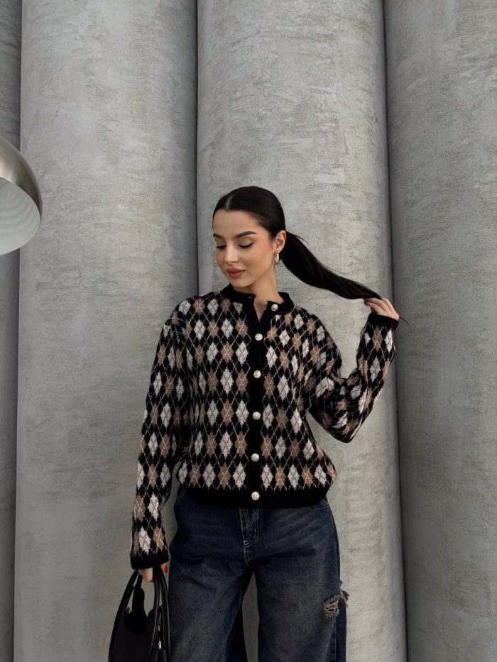 pitikare-ve-baklava-desenli-hirka-6 Ella Style pitikare ve baklava desenli siyah kadın hırka giyen bir kadın, bol kesim kot pantolon ve siyah çantayla kombin yapmış. Modern bir görünüm sağlayan gri beton sütunlar arka planda yer alıyor.