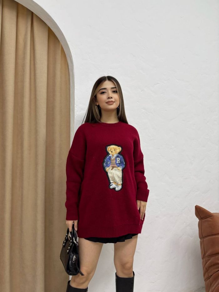 sevimli-ayicik-islemeli-oversize-kazak-1 Ayıcık işlemeli bordo oversize kazak giyen bir kadın. Siyah mini etek, siyah çizmeler ve siyah el çantası ile kombinlenmiş.
