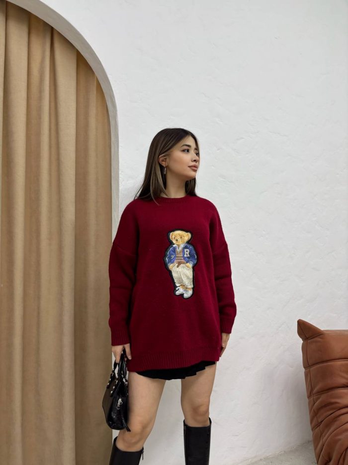 sevimli-ayicik-islemeli-oversize-kazak-2 Ayıcık işlemeli bordo oversize kazak giyen bir kadın. Siyah mini etek, siyah çizmeler ve siyah el çantası ile kombinlenmiş.