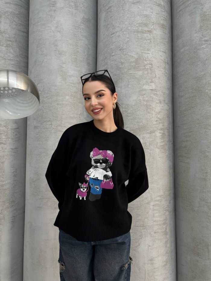 trend-ayicik-islemeli-siyah-oversize-kazak-3 Siyah renkte, üzerinde ayıcık işlemeli detay bulunan oversize kazak giyen bir kadın. Yırtık mavi kot pantolon ve gözlükle kombinlenmiş.