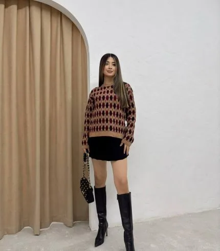 Baklava desenli bordo ve bej tonlarında yün kazak giyen bir kadın. Siyah mini etek, siyah çizme ve zincir detaylı siyah çantayla kombinlenmiş.