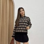 Baklava desenli bordo ve bej tonlarında yün kazak giyen bir kadın. Siyah mini etek, siyah çizme ve zincir detaylı siyah çantayla kombinlenmiş.