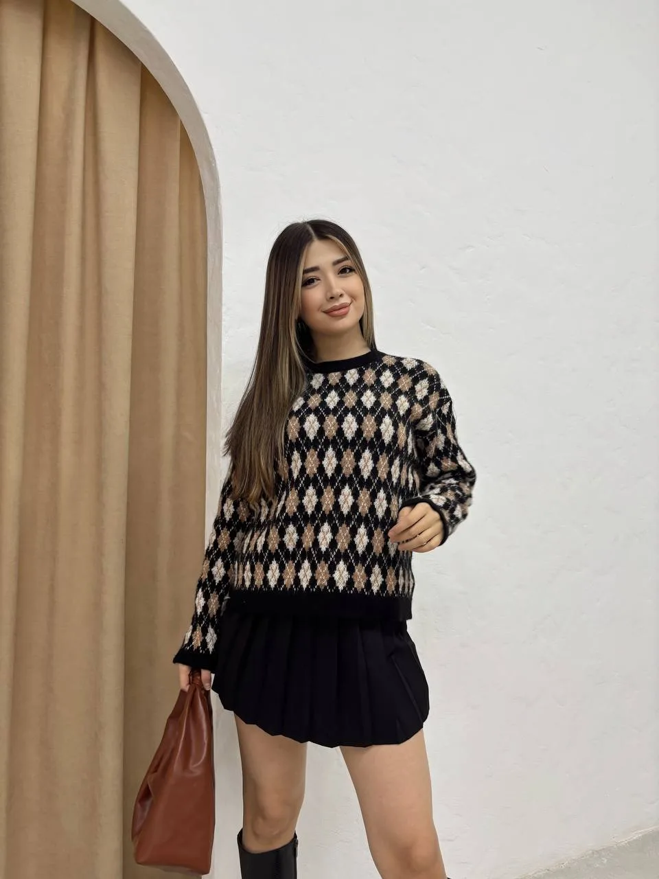 Baklava desenli bordo ve bej tonlarında yün kazak giyen bir kadın. Siyah mini etek, siyah çizme ve zincir detaylı siyah çantayla kombinlenmiş.
