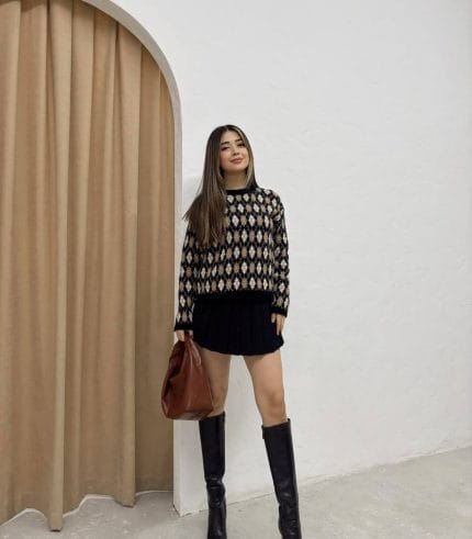 Baklava desenli bordo ve bej tonlarında yün kazak giyen bir kadın. Siyah mini etek, siyah çizme ve zincir detaylı siyah çantayla kombinlenmiş.