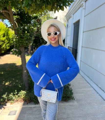 bisiklet yaka yumuşak dokulu krem rengi kazak giyen ve siyah tayt ile uzun çizmelerle kombinleyen bir kadın.