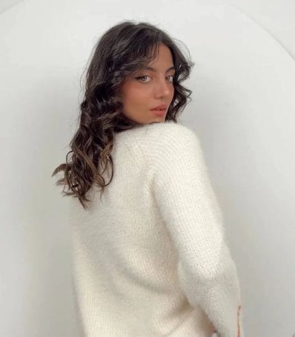 bisiklet yaka yumuşak dokulu krem rengi kazak giyen ve siyah tayt ile uzun çizmelerle kombinleyen bir kadın.