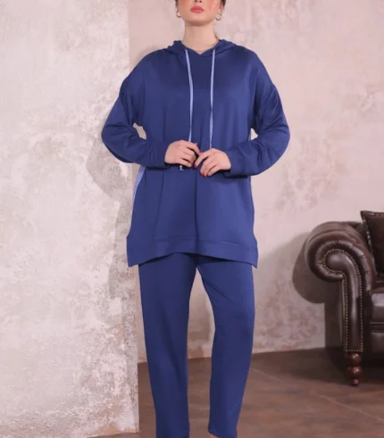 Doğal tonlarda tasarlanmış iç mekânda Oysho kumaş ikili takım giyen kadın. Kapüşonlu üst ve rahat kesim pantolonla şık bir kombin.