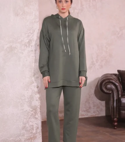 Doğal tonlarda tasarlanmış iç mekânda Oysho kumaş ikili takım giyen kadın. Kapüşonlu üst ve rahat kesim pantolonla şık bir kombin.