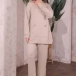 Doğal tonlarda tasarlanmış iç mekânda Oysho kumaş ikili takım giyen kadın. Kapüşonlu üst ve rahat kesim pantolonla şık bir kombin.